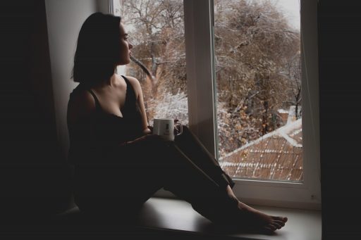 Vrouw die bij een raam zit op een bewolkte herfstdag en naar buiten kijkt